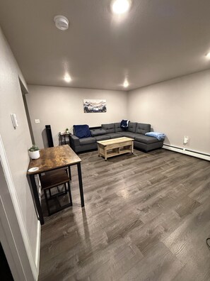 Un soggiorno con un divano grigio, un tavolino in legno e un quadro appeso al muro.