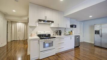 A modern kitchen with white cabinetry, stainless steel appliances, and a wooden floor.