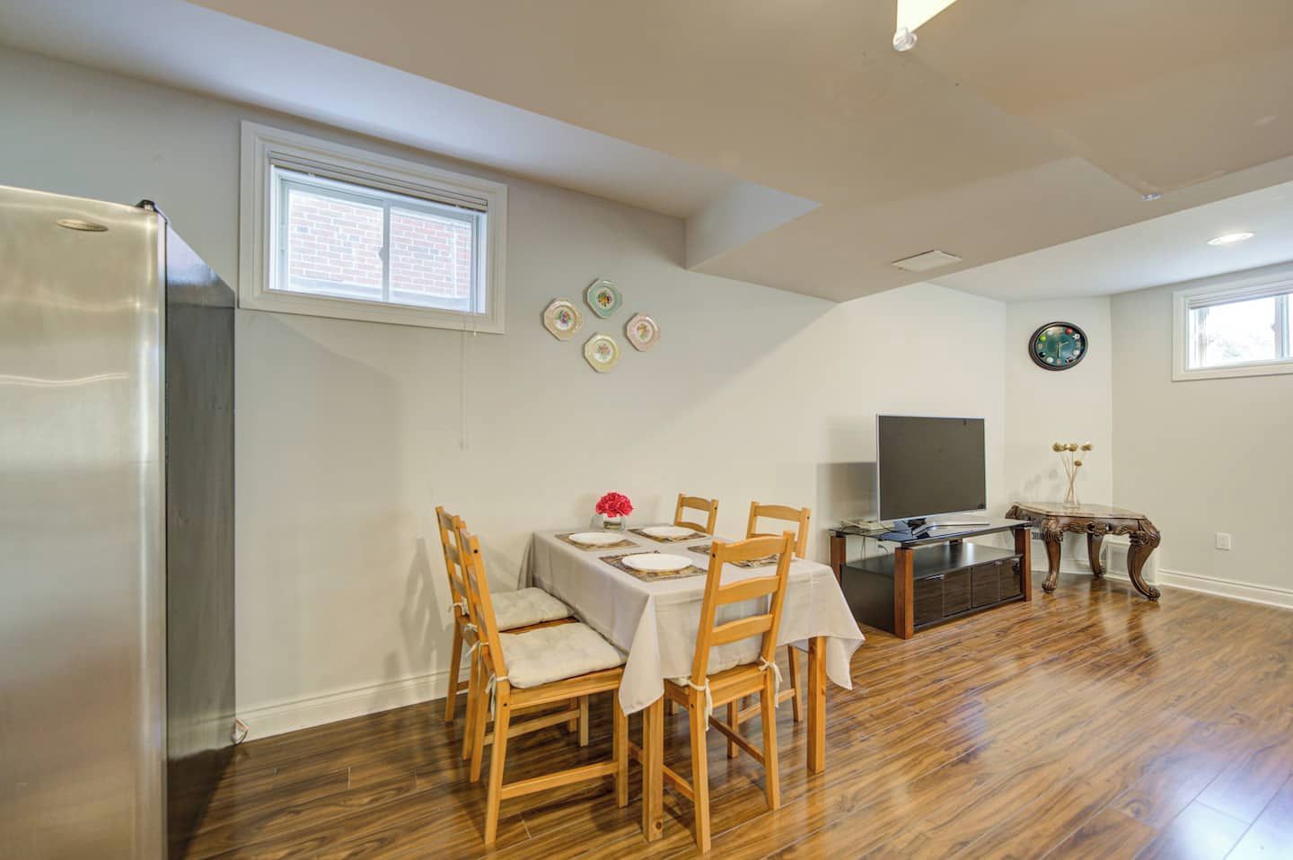 Un coin repas avec une table dressée pour quatre personnes, un téléviseur et une horloge au mur.