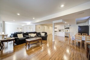A spacious living area with a black leather sofa, a wooden coffee table, and a dining area with a wooden table and chairs.