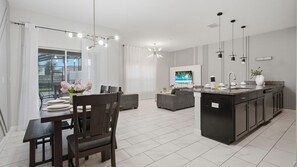 Une cuisine moderne dotée d’un îlot central, un coin repas avec une table et des chaises, et un espace de vie comprenant un canapé et un téléviseur.
