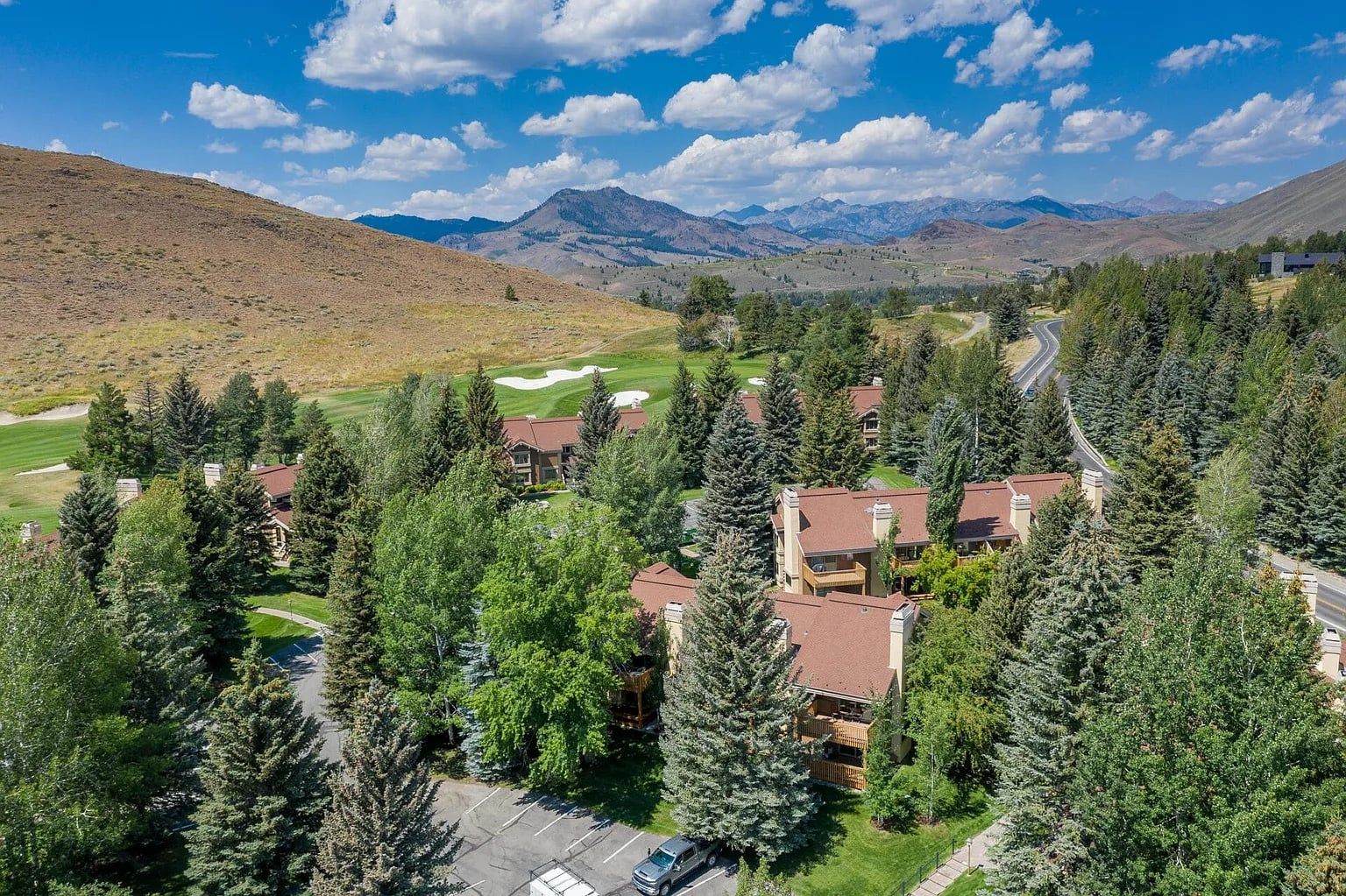 Un barrio residencial con casas rodeadas de árboles, un campo de golf y montañas al fondo.