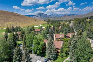 Un barrio residencial con casas rodeadas de árboles, un campo de golf y montañas al fondo.