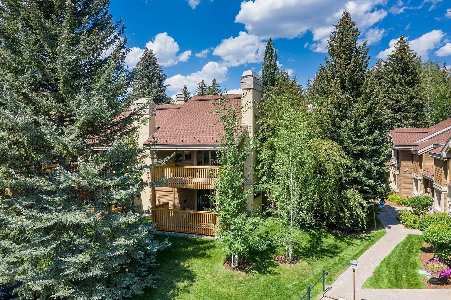 A residential building with a balcony, surrounded by evergreen trees and a well-maintained lawn.