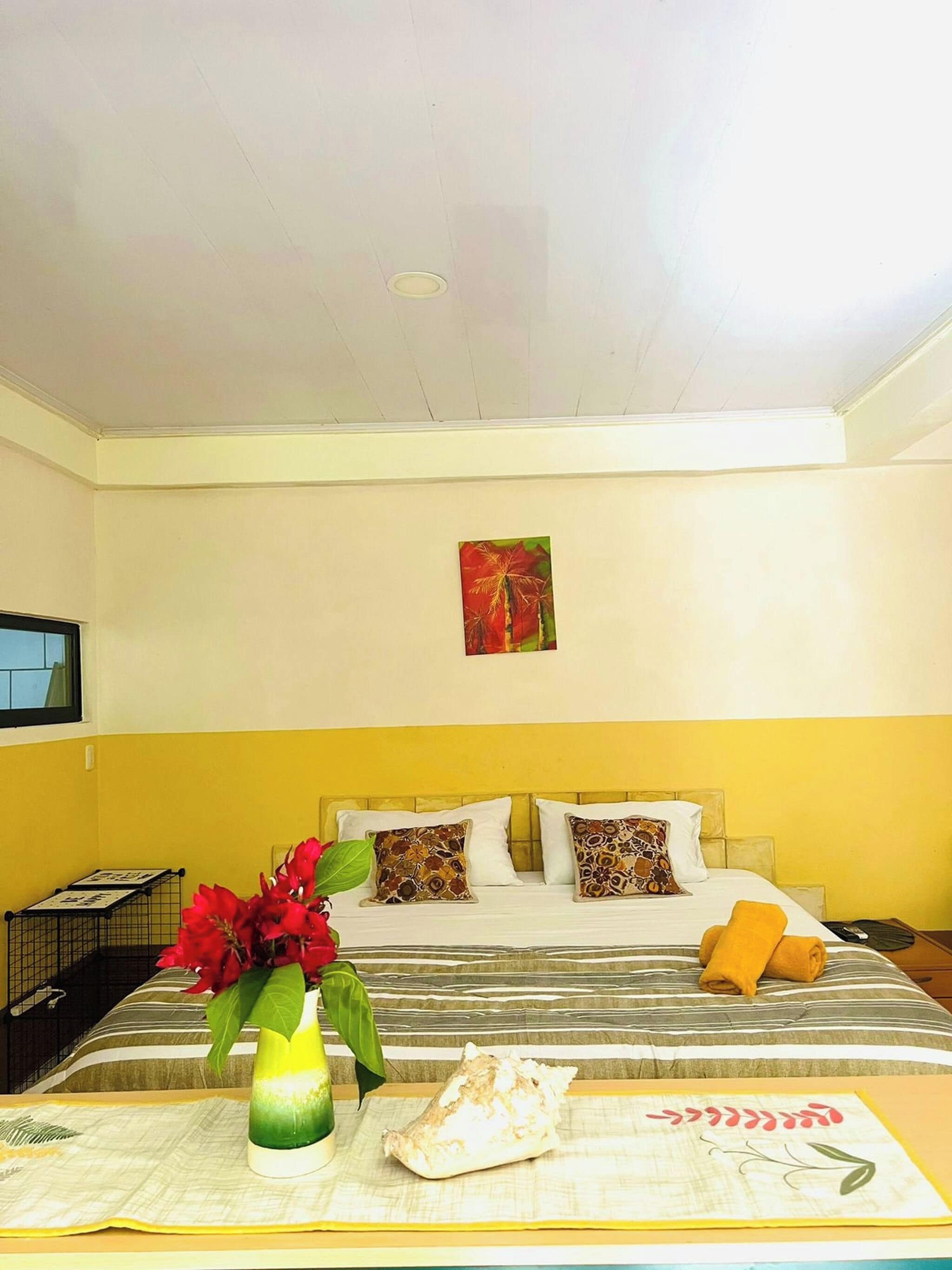 A hotel room with a bed, a wall-mounted TV, a painting, and a vase with flowers.