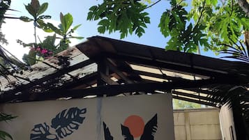Una habitación con un mural de hojas y un sol, un ventilador y una lavadora.