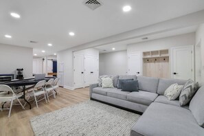 A modern living room with a grey sofa, a dining table with chairs, and a kitchen area in the background. - Poconos Masthope 4BR Home Ski Big Bear - Lake Pool (Lackawaxen)