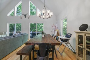A spacious dining area with a large wooden table, multiple chairs, and a bench. There are two large windows providing natural light and views of the outdoors. - Poconos Masthope 4BR Home Ski Big Bear - Lake Pool (Lackawaxen)