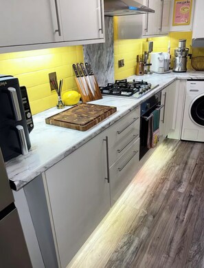 A kitchen with a gas stove, a washing machine, and a cutting board. - Luxury Leith Apartment | Stylish Edinburgh Stay (Edinburgh)