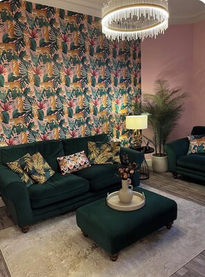 A living room with a green sofa, patterned wallpaper, a chandelier, and a side table with a lamp. - Luxury Leith Apartment | Stylish Edinburgh Stay (Edinburgh)