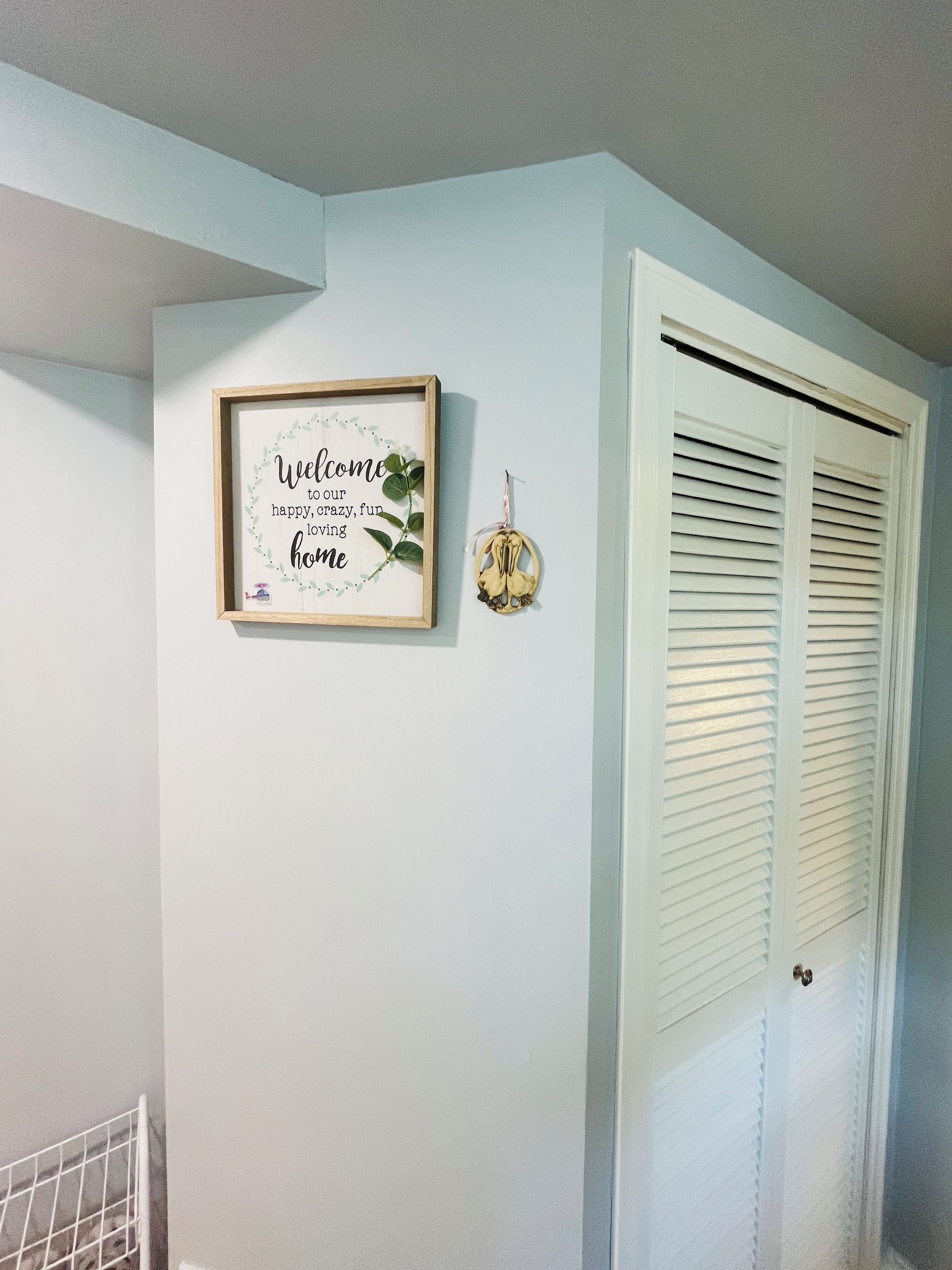 A framed welcome sign with a quote, a small decorative item, and a white door with shutters.