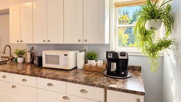A kitchen with white cabinets, a microwave, a coffee maker, and a window with a plant.