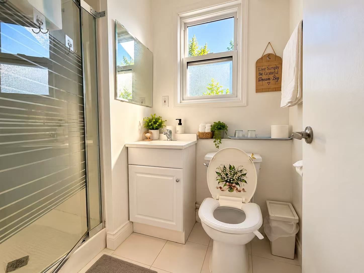 Ein Badezimmer mit Toilette, Waschbecken und Duschbereich. Ein Fenster bietet Blick auf grüne Natur.