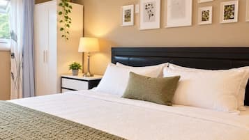 A neatly made bed with white linens and a green accent pillow, a bedside lamp, and a wall with framed artwork.