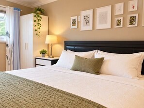 A neatly made bed with white linens and a green accent pillow, a bedside lamp, and a wall with framed artwork. - White Rock Suite + 3-min drive to the Beach (White Rock)