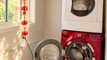 A laundry room with a red washing machine and a white dryer, a window with red lanterns, and a tiled floor.