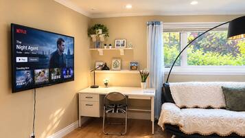 A room with a desk, chair, and a couch. A television mounted on the wall displays a Netflix show.