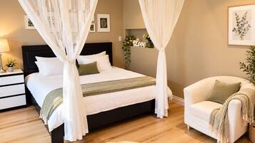 A bedroom with a four-poster bed, a bedside table with a lamp, a chair with a throw blanket, and a wall-mounted shelf with decorative items.