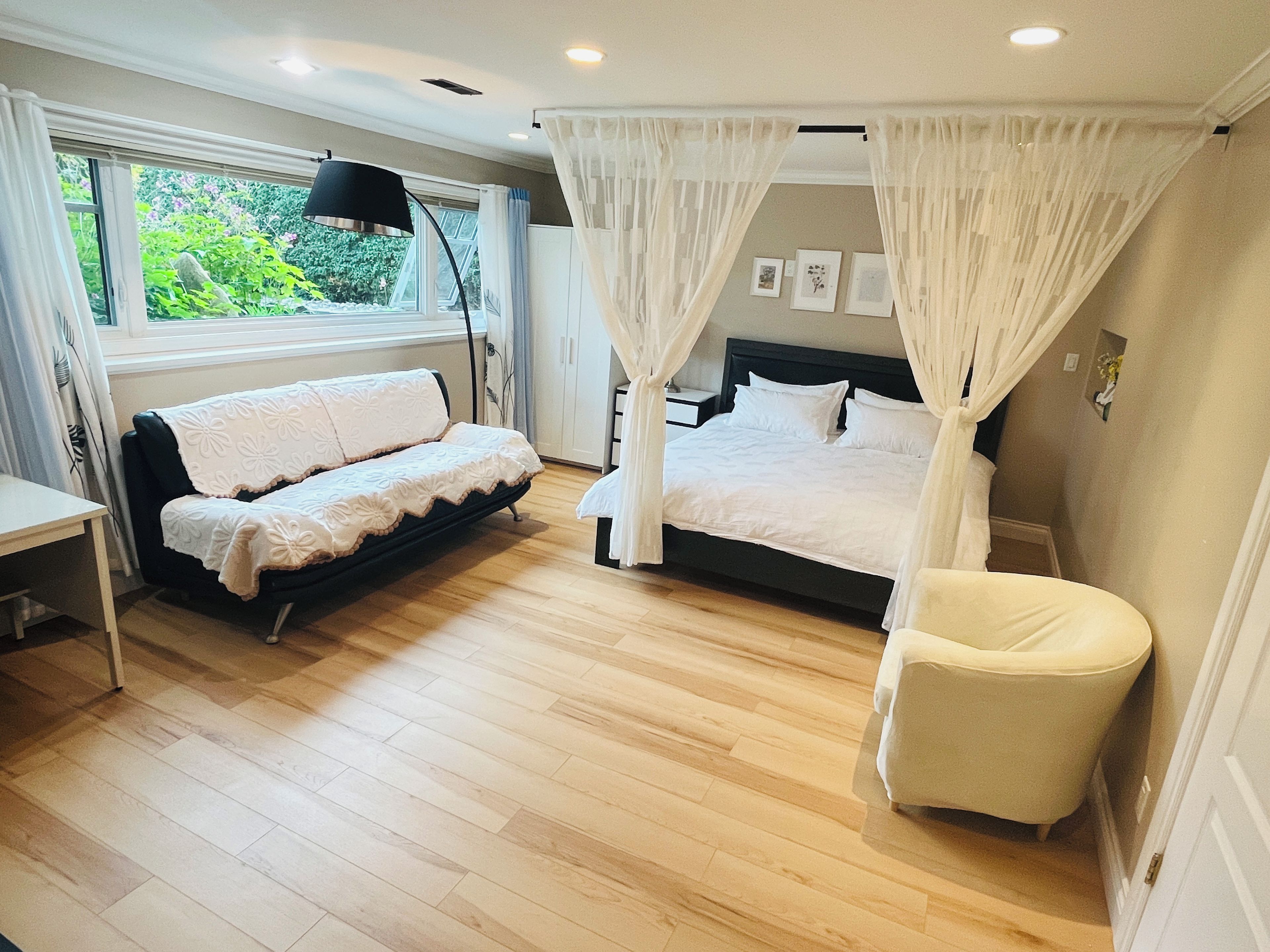 A bedroom with a bed, a sofa, a chair, a bedside table, and a window with curtains.