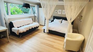 A bedroom with a bed, a sofa, a chair, a bedside table, and a window with curtains.
