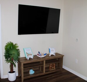 Une pièce comprenant une console en bois, une plante en pot, un panneau d’accueil, un livre d’or et un téléviseur à écran plat fixé au mur.