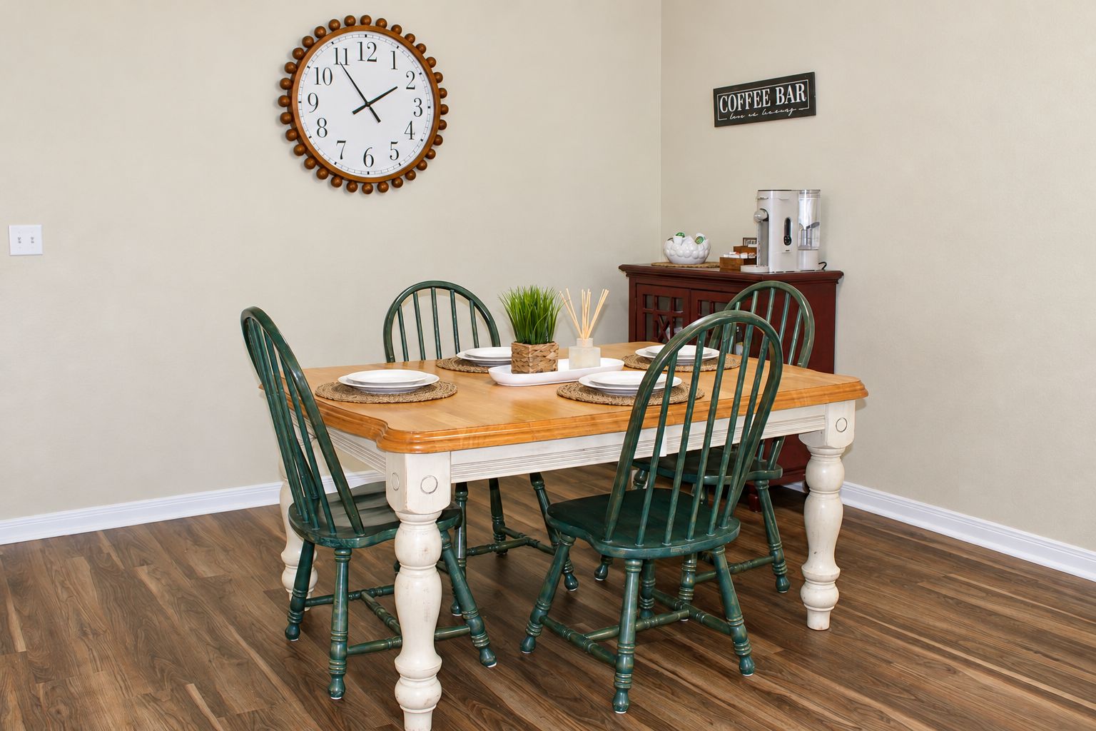 A dining room with a wooden table, four chairs, a clock, and a coffee bar sign.