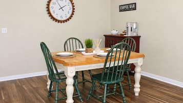 A dining room with a wooden table, four chairs, a clock, and a coffee bar sign.