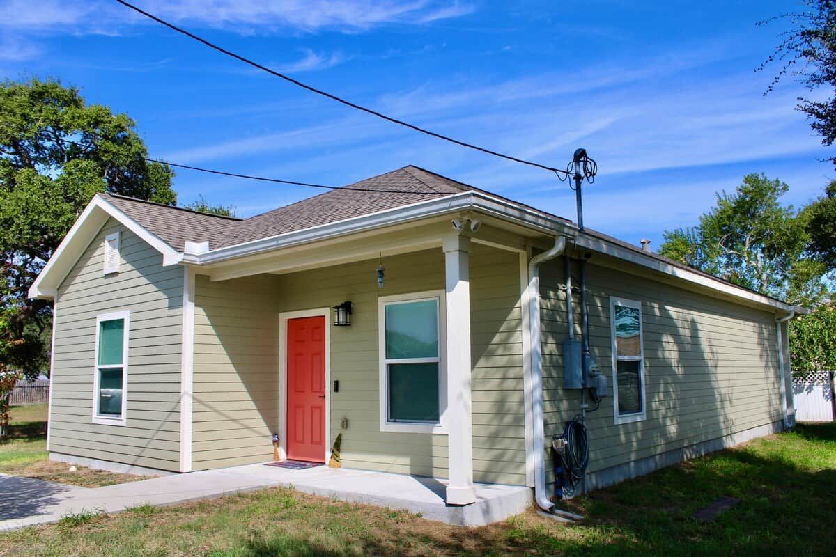 A single-story house with a red door, a covered porch, and a visible utility pole.