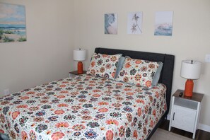 Une chambre à coucher avec une couvre-lit à motifs floraux, deux tables de chevet avec des lampes et trois tableaux encadrés accrochés au mur.
