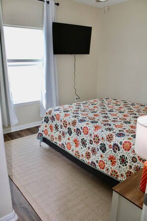 A bedroom with a bed, a television mounted on the wall, and a window with curtains. - Casita del Mar, a Charming coastal getaway (Rockport)