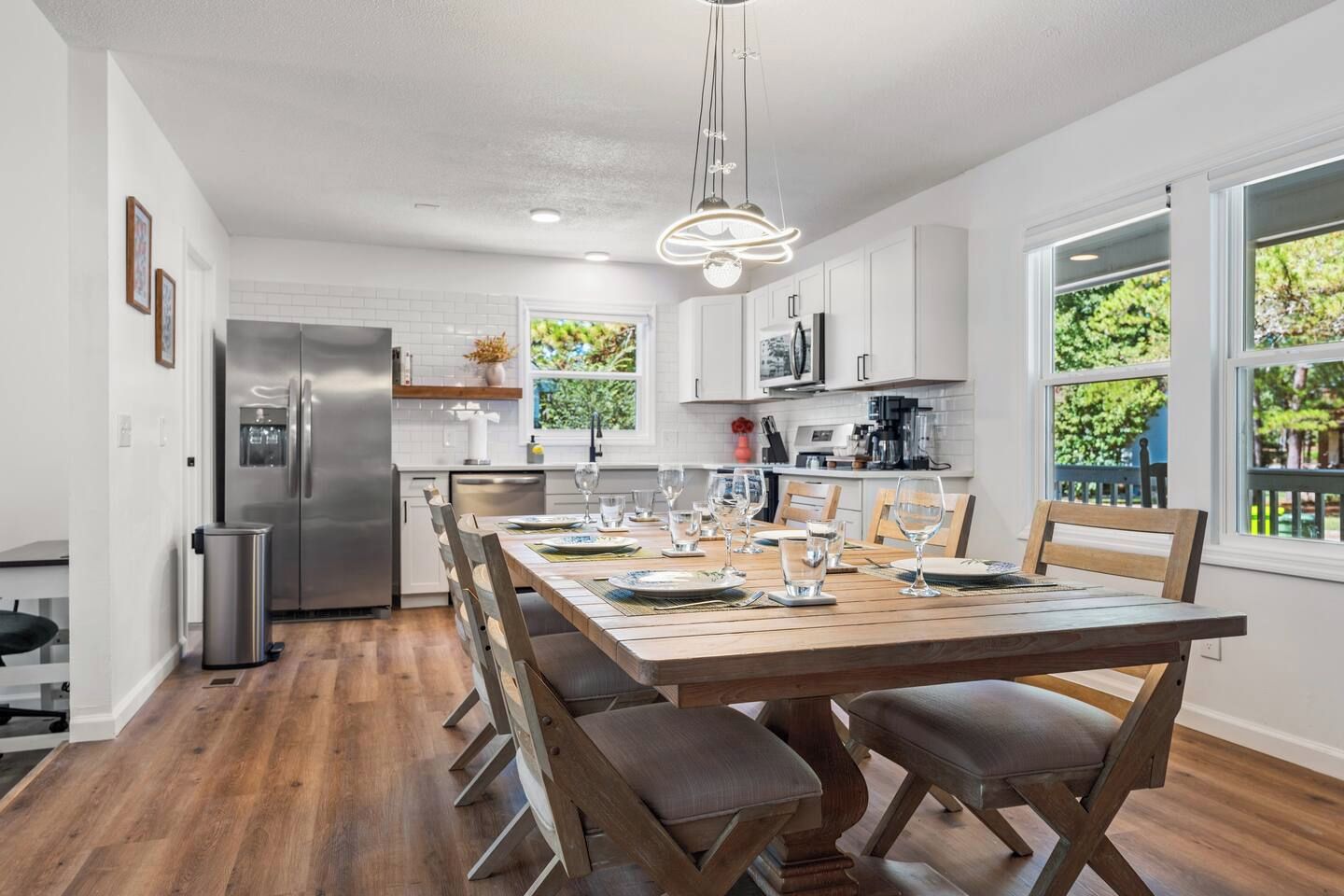 A modern kitchen with white cabinets, a stainless steel refrigerator, and a dining area with a wooden table set for four.