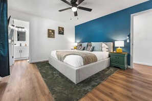Un dormitorio con cama, mesitas de noche, ventilador de techo y una puerta que da a un baño.
