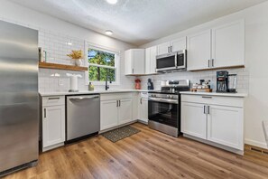A modern kitchen with white cabinetry, stainless steel appliances, and a wooden floor. - Luxury Spacious Columbia Stay | 3BR • 2BA (Columbia)
