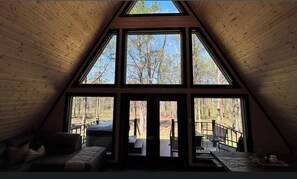 A room with a sloped ceiling, large windows, a sofa, and a deck area.