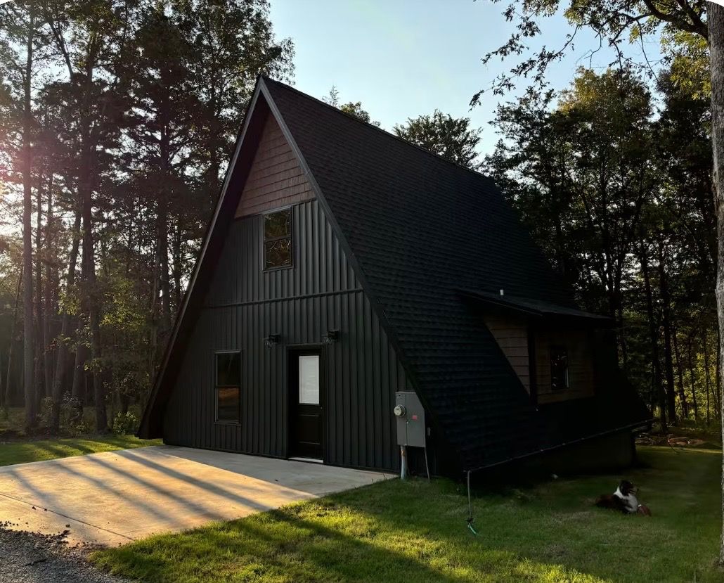 Une cabane moderne, aux couleurs sombres et dotée d’un toit en pente, entourée d’arbres.