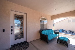 A covered porch with a door, a wicker chair, and a matching ottoman. - Lake Havasu Getaway w/ Boat Parking & Pool - Sleeps 10! (Lake Havasu City)