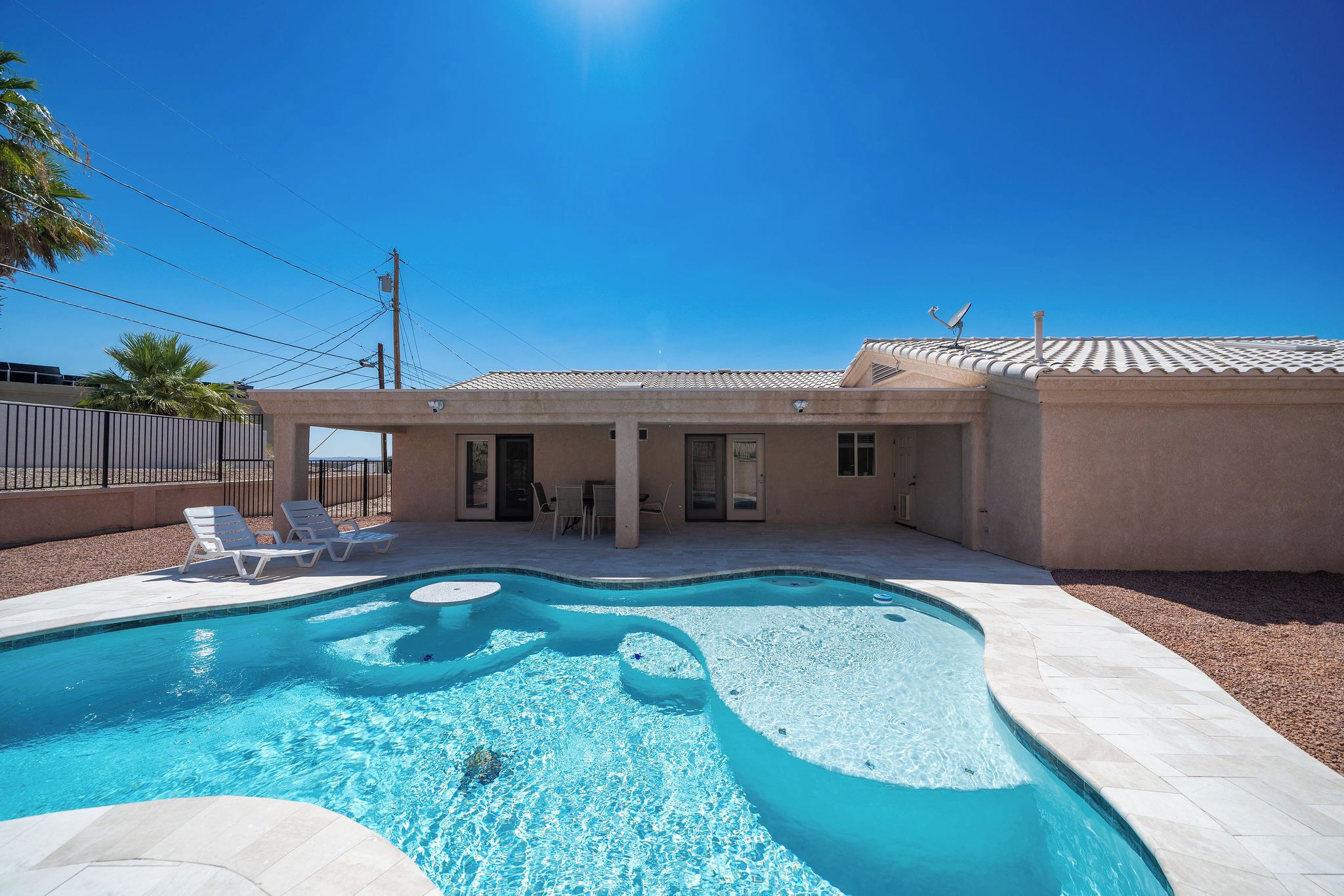 A swimming pool with a curved design, surrounded by a patio area with lounge chairs.
