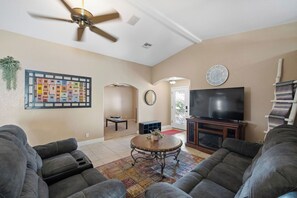 A living room with a ceiling fan, a flat-screen TV, a fireplace, and a large rug. - Lake Havasu Getaway w/ Boat Parking & Pool - Sleeps 10! (Lake Havasu City)