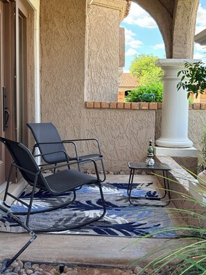 Un espacio de estar al aire libre cubierto con una silla de metal negro, una mesita y una alfombra estampada.