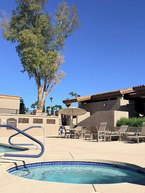 Un área de piscina con sillas de descanso, una pérgola y un árbol grande.