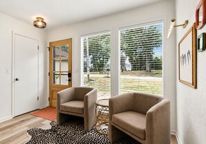 Quarto com duas poltronas, uma mesa redonda pequena e uma porta que dá para o exterior.