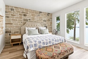 A bedroom with a stone wall, a bed with patterned bedding, a wooden nightstand, and a window with blinds. - FOUR bedroom FOUR bathroom - HOT TUB! - One entire separate garage en-suite !! (Sunrise Beach)