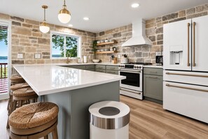 A modern kitchen with a large island, stone walls, and a view of the outdoors. - FOUR bedroom FOUR bathroom - HOT TUB! - One entire separate garage en-suite !! (Sunrise Beach)