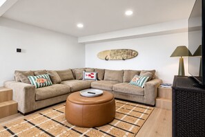 Ein modernes Wohnzimmer mit einem Ecksofa, einem runden Hocker und einem Flachbildfernseher.