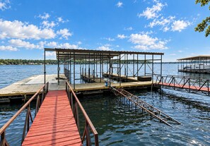 Eine hölzerne Mole führt ins ruhige Wasser, mit einer überdachten Sitzgelegenheit und einem Boot im Hintergrund.