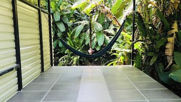 A covered patio area with a hammock, tiled flooring, and lush tropical plants.