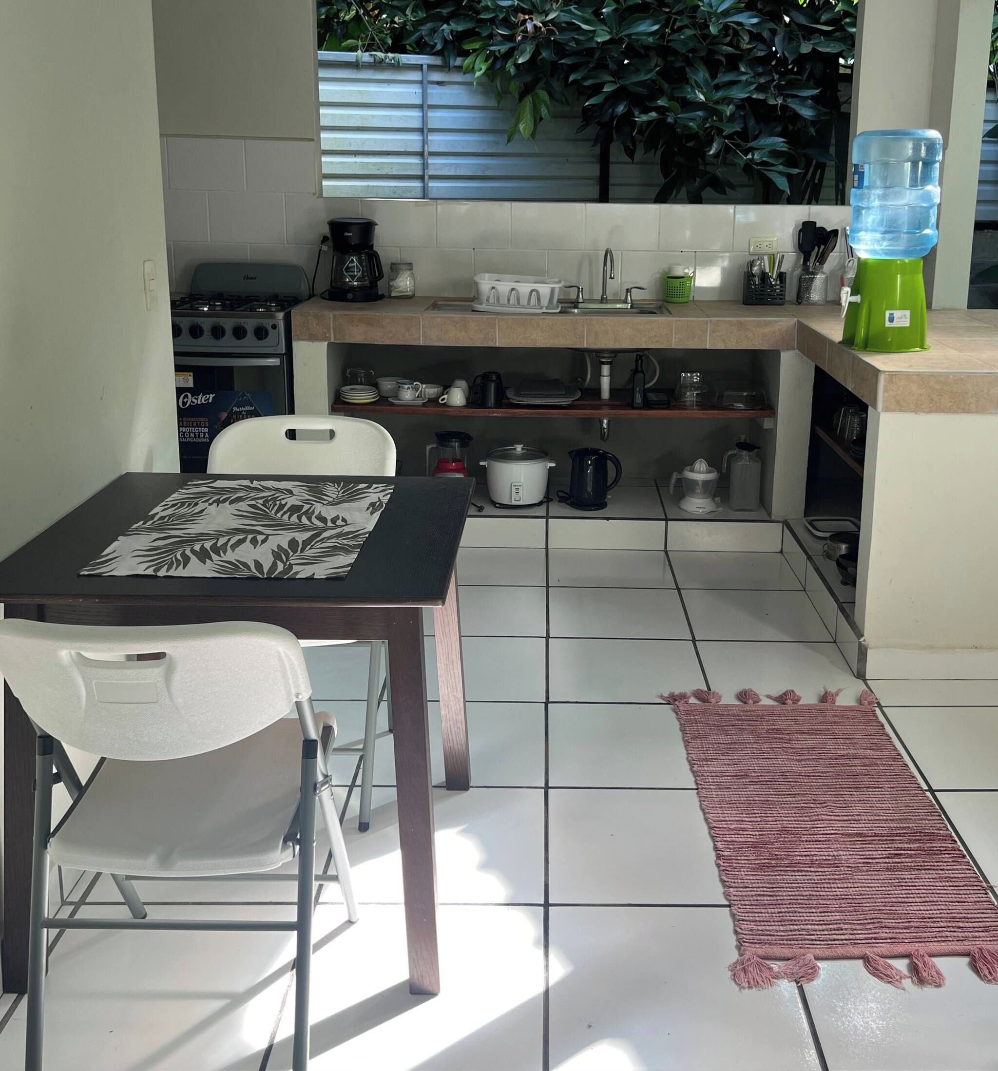 A compact kitchen with a gas stove, coffee maker, and various kitchenware on shelves.
