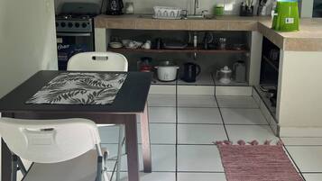 A compact kitchen with a gas stove, coffee maker, and various kitchenware on shelves.