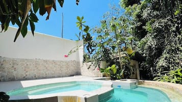 A swimming pool with a curved edge, surrounded by stone steps and a white wall.