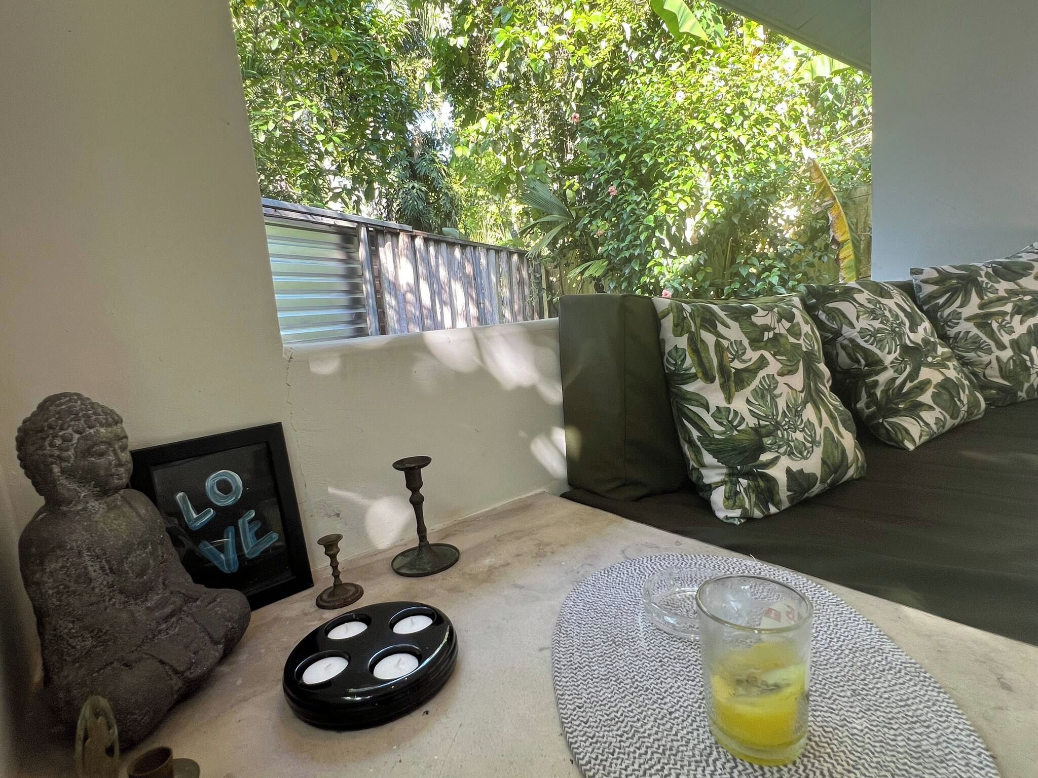 A room with a sofa, cushions, a statue, a framed picture, a candle holder, and a glass with a yellow liquid.